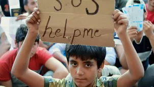 Ni&ntilde;o inmigrante sostiene un cartel en el que se lee &#039;SOS ay&uacute;dame&#039; mientras se sienta con otros migrantes en Keleti. (V&iacute;a: AFP)