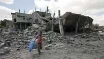 Un ni&ntilde;o palestino carga una pelota y una jaula de p&aacute;jaro mientras camina por los escombros de un edificio cerca al centro de refugiados de Rafah, al sur de Gaza. (Foto: AFP)